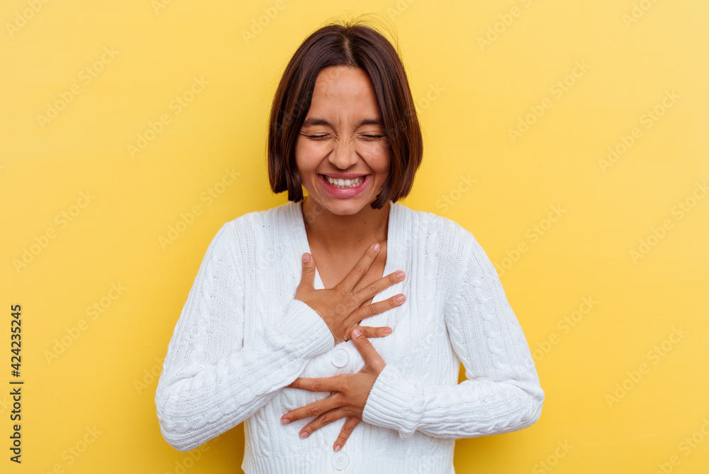 Young mixed race woman isolated on yellow background laughs happily and has fun keeping hands on stomach. Young mixed race woman isolated on yellow background laughs happily and has fun keeping hands on stomach.