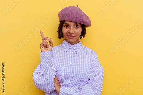 Young mixed race woman wearing a beret isolated on yellow background smiling cheerfully pointing with forefinger away.
