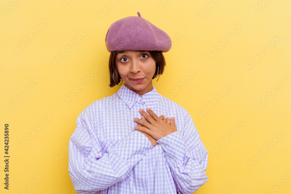 Young mixed race woman wearing a beret isolated on yellow background laughing keeping hands on heart, concept of happiness. Young mixed race woman wearing a beret isolated on yellow background laughing keeping hands on heart, concept of happiness.