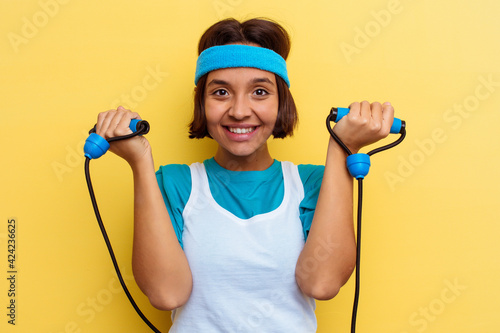 Young sport mixed race woman holding an elastic rope isolated on yellow background