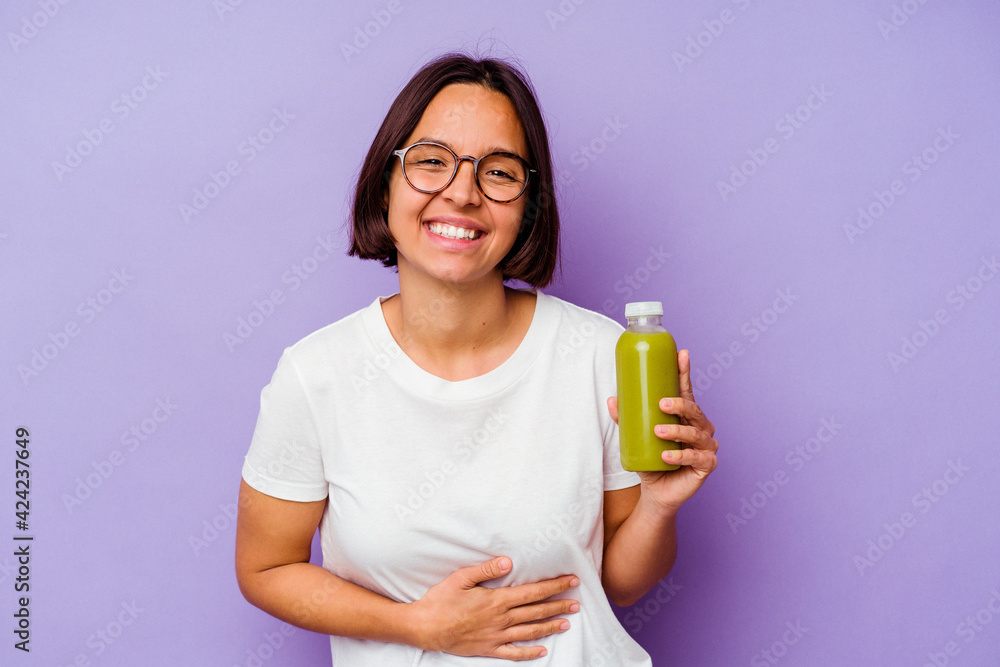 Young mixed race woman holding a healthy smoothie isolated on purple background laughing and having fun. Young mixed race woman holding a healthy smoothie isolated on purple background laughing and having fun.