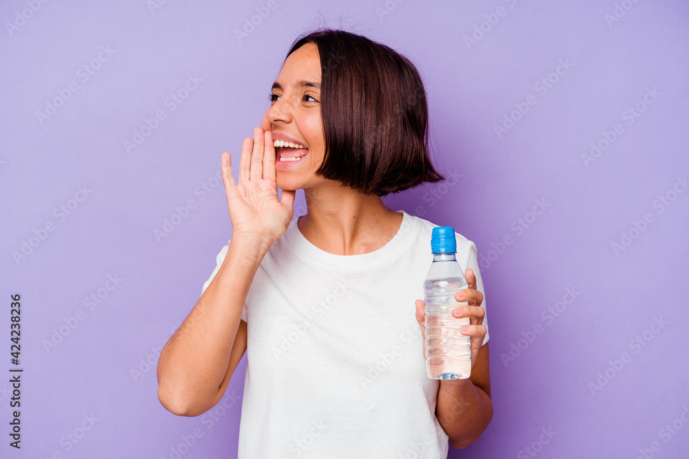 Young mixed race holding a water bottle isolated on purple background shouting and holding palm near opened mouth. Young mixed race holding a water bottle isolated on purple background shouting and holding palm near opened mouth.