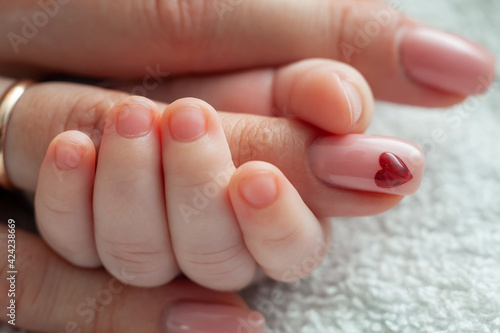 Infant holding mommy's finger. Mum taking care of the infant baby. Heart sign on mom's nail. Family, motherhood, love concept.