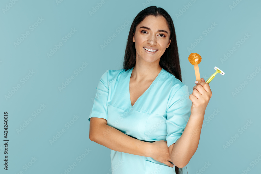 Smiling cosmetologist holding sugaring paste and razor for depilation procedure over blue background. Smiling cosmetologist holding sugaring paste and razor for depilation procedure over blue background.