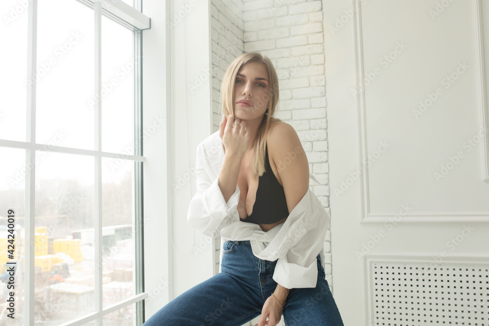 Young sexy blonde woman on the sofa in black bra and men's white shirt.  Stock Photo