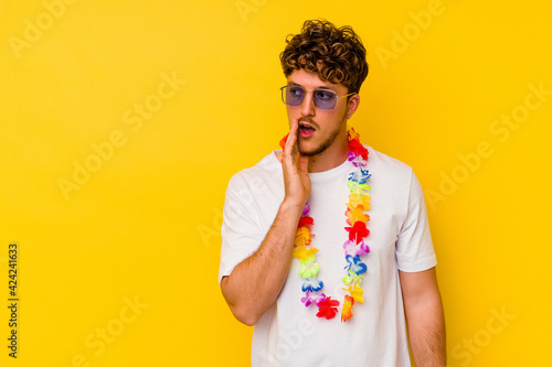 Young caucasian man wearing a Hawaiian party stuff isolated on yellow background is saying a secret hot braking news and looking aside