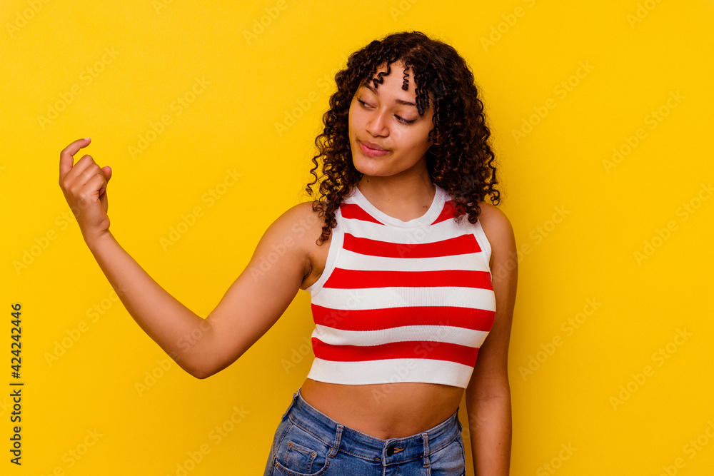 Young mixed race woman isolated on yellow background pointing with finger at you as if inviting come closer. Young mixed race woman isolated on yellow background pointing with finger at you as if inviting come closer.
