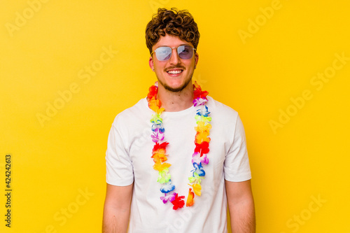 Young caucasian man wearing a Hawaiian party stuff isolated on yellow background happy, smiling and cheerful.