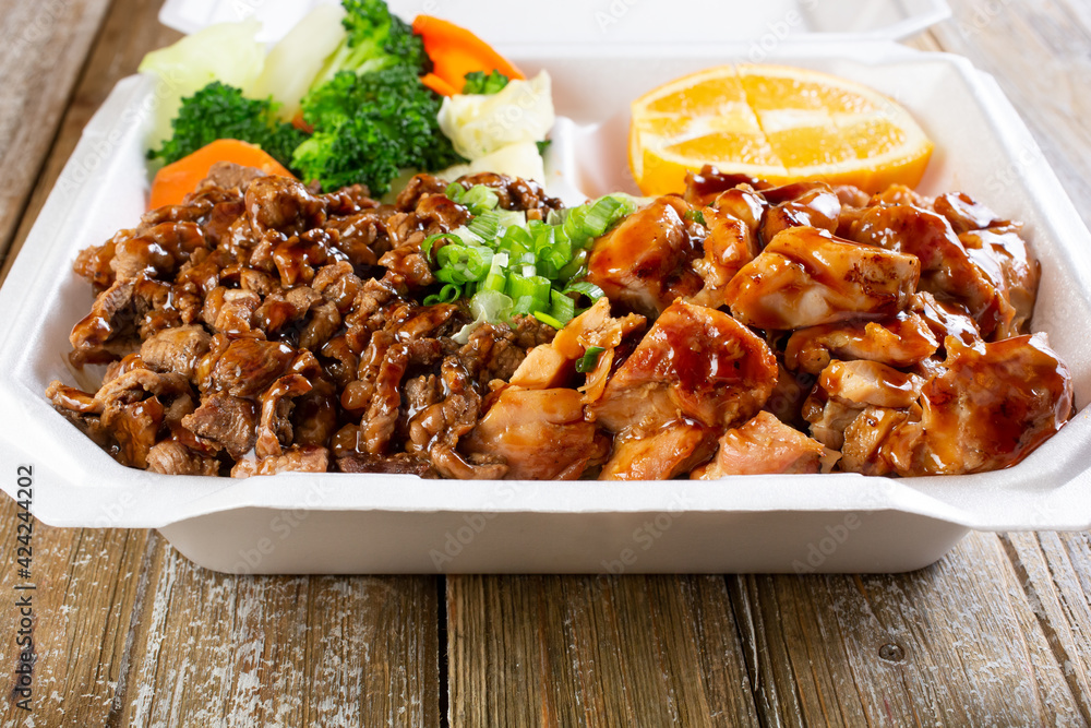 A closeup view of a to-go container featuring beef and chicken teriyaki over rice. A closeup view of a to-go container featuring beef and chicken teriyaki over rice.