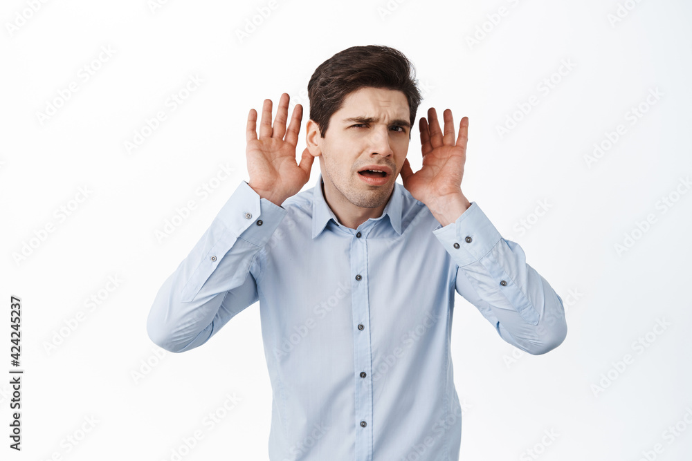 What I cant hear you. Confused male office manager, holding hands near ears and looking puzzled, listening closer, trying to eavesdrop, standing against white background What I cant hear you. Confused male office manager, holding hands near ears and looking puzzled, listening closer, trying to eavesdrop, standing against white background