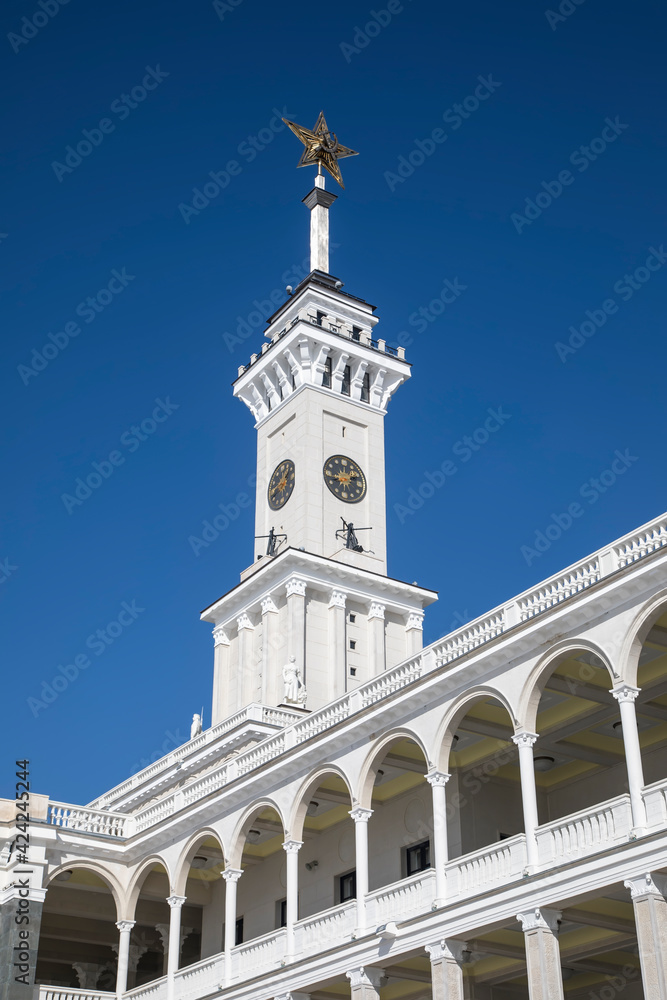 A beautiful tower with a clock and a star on the spire. Blue sky. Old Soviet architecture. Gold star on the spire of the building. Sunny day.
