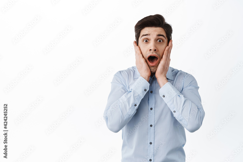 Shocked and startled caucasian man gasping, holding hands on cheeks and stare speechless at camera, standing in awe against white background Shocked and startled caucasian man gasping, holding hands on cheeks and stare speechless at camera, standing in awe against white background
