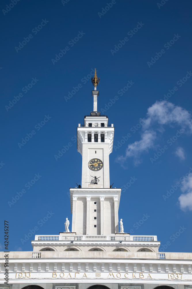 A beautiful tower with a clock and a star on the spire. Blue sky. Old Soviet architecture. Gold star on the spire of the building. Sunny day.