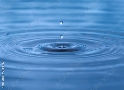 Water droplet dripping into blue pool creating ripples and abstract shape of water. Darkest area in center is in camera focus. Image contains some grain, noise and motion blur