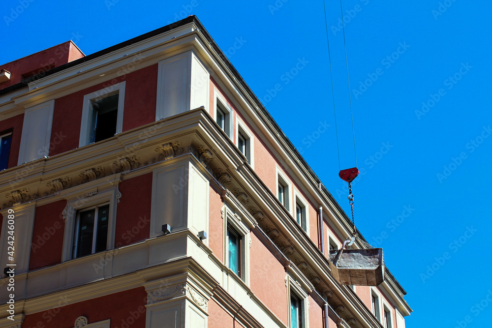 Fototapeta premium Renovation works in a residential area of Rome, a crane transports cargo, residential buildings and blue sky.