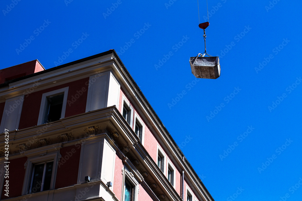Renovation works in a residential area of ​​Rome, a crane transports cargo, residential buildings and blue sky.