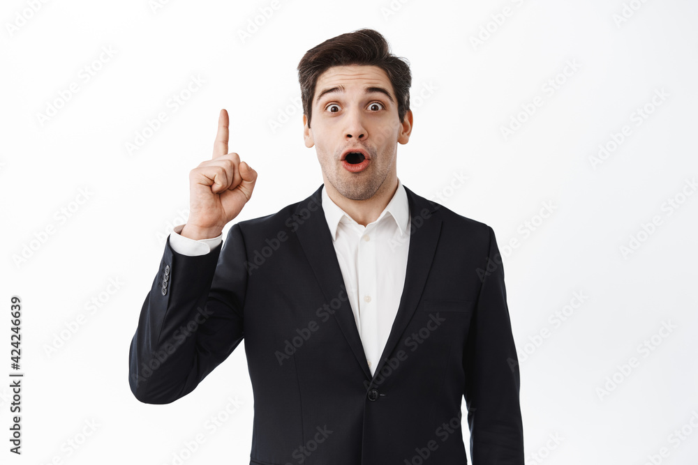 Excited businessman raise index finger, pitching an idea, think up solution, perfect plan, say suggestion, standing over white background in black suit Excited businessman raise index finger, pitching an idea, think up solution, perfect plan, say suggestion, standing over white background in black suit