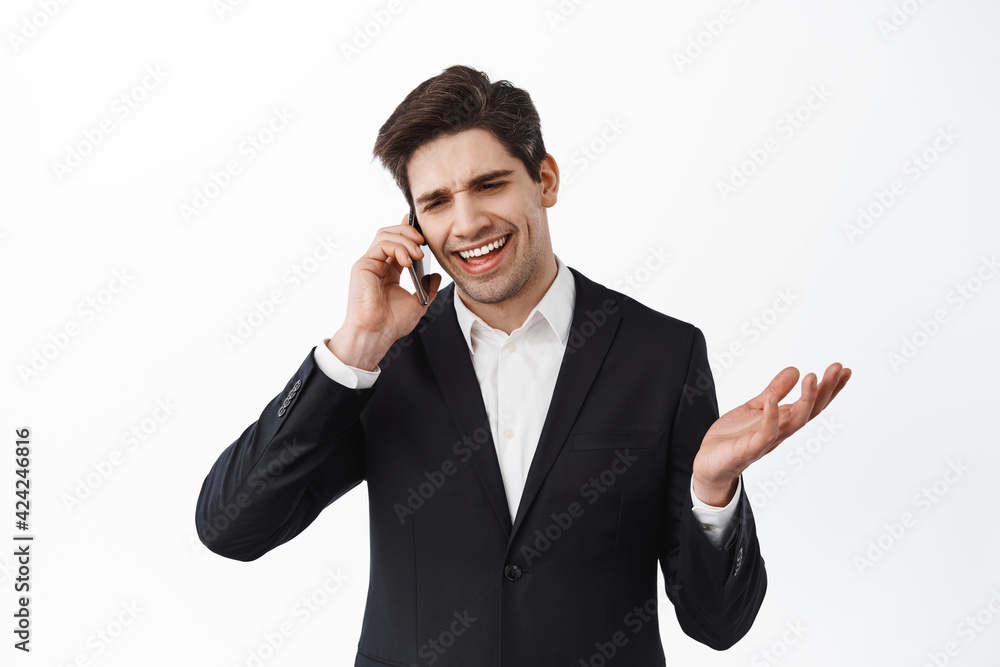 Handsome businessman having business call on mobile phone, smiling and saying yes, give approval, looking satisfied during conversation, white background Handsome businessman having business call on mobile phone, smiling and saying yes, give approval, looking satisfied during conversation, white background