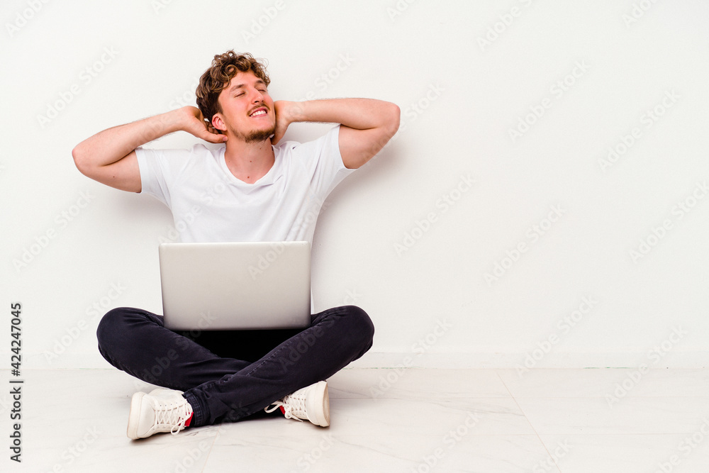 Young caucasian man sitting on the floor holding on laptop isolated on white background stretching arms, relaxed position. Young caucasian man sitting on the floor holding on laptop isolated on white background stretching arms, relaxed position.