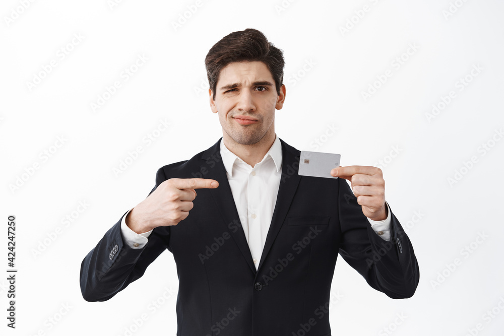 Disappointed business man in suit points at bad credit card, frowning upset or doubtful, judging awful banking, standing over white background Disappointed business man in suit points at bad credit card, frowning upset or doubtful, judging awful banking, standing over white background