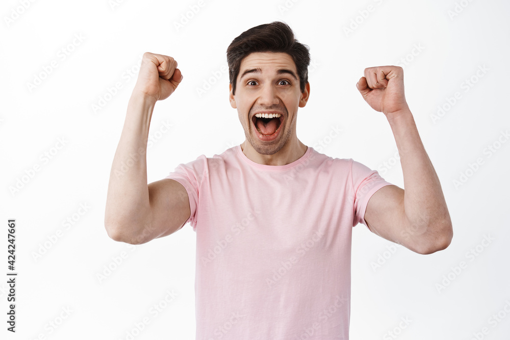 Happy celebrating man scream from joy and happiness, shaking hands in rejoice and celebration, winning, triumphing of victory, standing over white background Happy celebrating man scream from joy and happiness, shaking hands in rejoice and celebration, winning, triumphing of victory, standing over white background