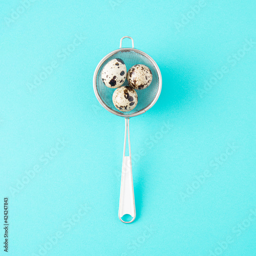 Quail eggs in colande. Minimal Easter concept on bright blue background photo