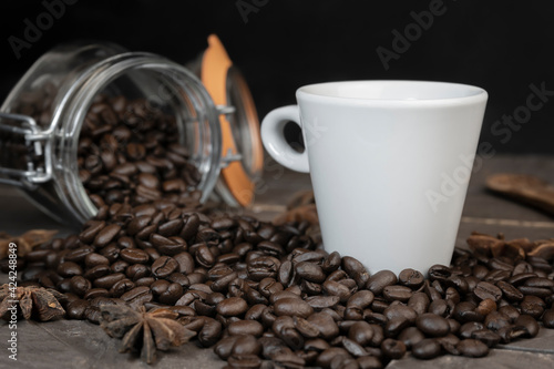Coffee beans in glass jar with a white coffee cup.Concept of energy caffeine drink on dark background.