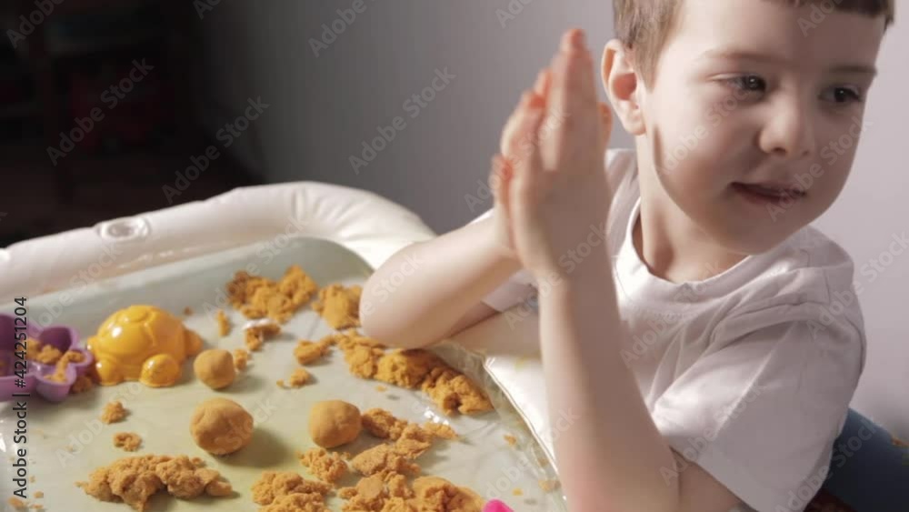 A boy sit At White Table And Play With Kinetic Sand at home. A child in a white T-shirt plays educational games. Development of fine motor skills and sensory perception. High quality FullHD footage A boy sit At White Table And Play With Kinetic Sand at home. A child in a white T-shirt plays educational games. Development of fine motor skills and sensory perception. High quality FullHD footage