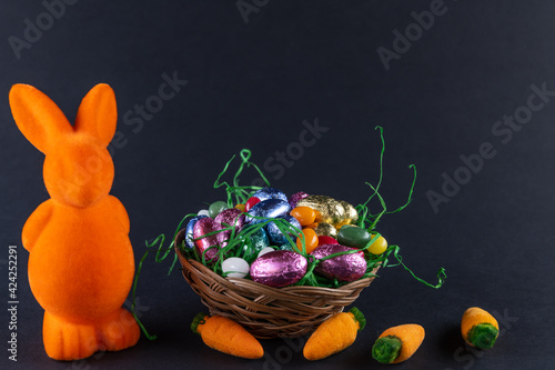 Orangefarbener Hase mit Möhren und einen gefüllten Osternest mit süßen Eiern auf schwarzem Untergrund photo