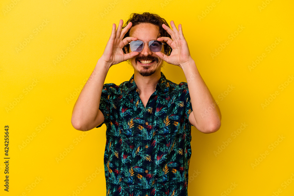 Young caucasian man wearing summer clothes isolated on yellow background showing okay sign over eyes Young caucasian man wearing summer clothes isolated on yellow background showing okay sign over eyes