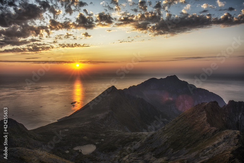 Amazing sunset over calm waters of Norwegian Sea. Mountain cliffs at foreground. Flares. Tourism, travel concept. Background. Copy space.