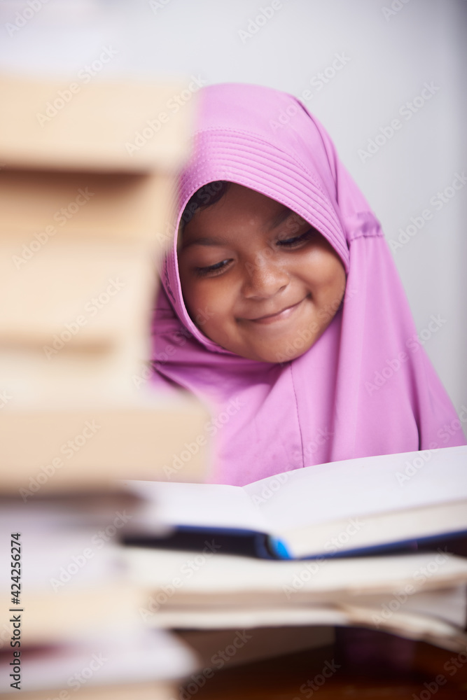 Little muslim girl in hijab reading a book and study at home Little muslim girl in hijab reading a book and study at home