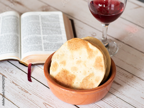 Unleavened bread with a glass of red wine cup for Passover Festival celebration with opened Bible on wooden table. Lord commandment to worship on Holy Day Pesach in exodus.