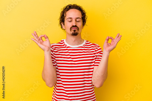 Young caucasian man isolated on yellow background relaxes after hard working day, she is performing yoga.
