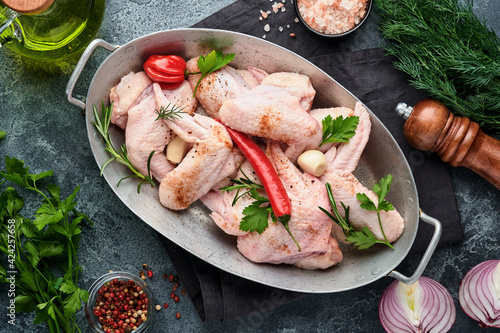 Raw chicken wings in metal pan or bowl with spices and ingredients for cooking on dark grey slate, stone or concrete background. Raw meat with spices at black table. Top view. Mock up.