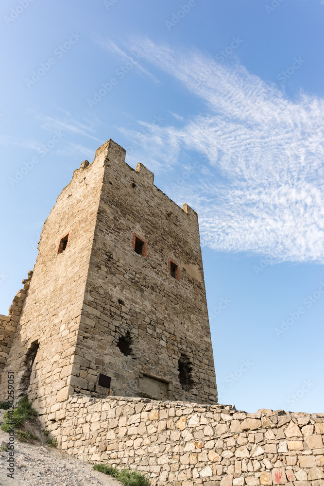 Bottom-up view of the stone wall and the defensive tower of Clement of the medieval fortress Kafa. Blue sky with cirrus clouds