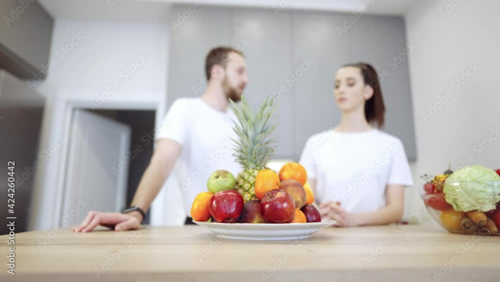 Young cheerful couple in the kitchen. There are fruits and vegetables on the wooden table. They discuss healthy food, vegan nutrition. Young cheerful couple in the kitchen. There are fruits and vegetables on the wooden table. They discuss healthy food, vegan nutrition.