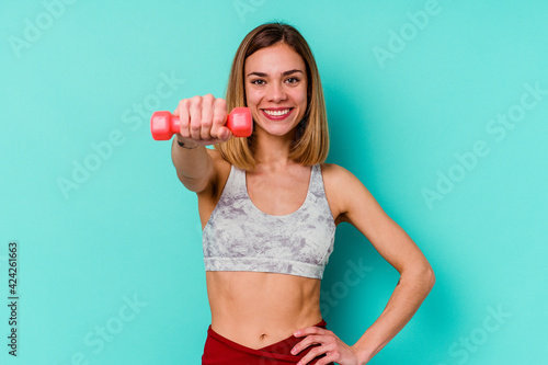 Young sport skinny caucasian holding a dumbbell woman isolated on blue background