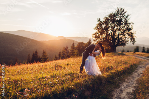 Beautiful newlyweds couple hugging in mountains at sunset. Bride and groom walking in summer Carpathians.
