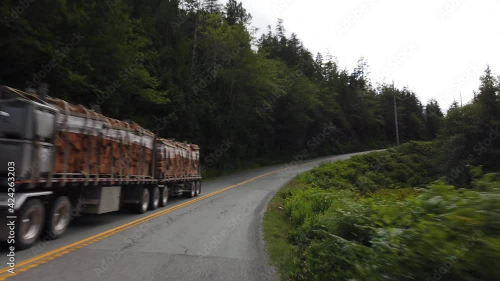 Slow motion gimbal driving shot of a truck full of tree logs during summer Slow motion gimbal driving shot of a truck full of tree logs during summer
