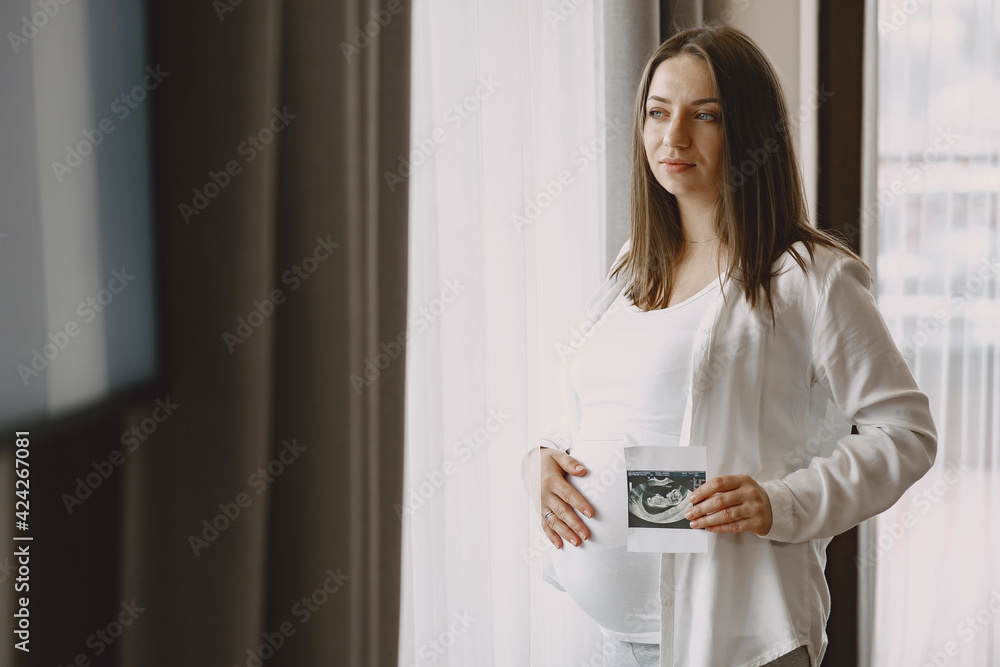 Pregnant woman stands by the window and looks at photo Pregnant woman stands by the window and looks at photo