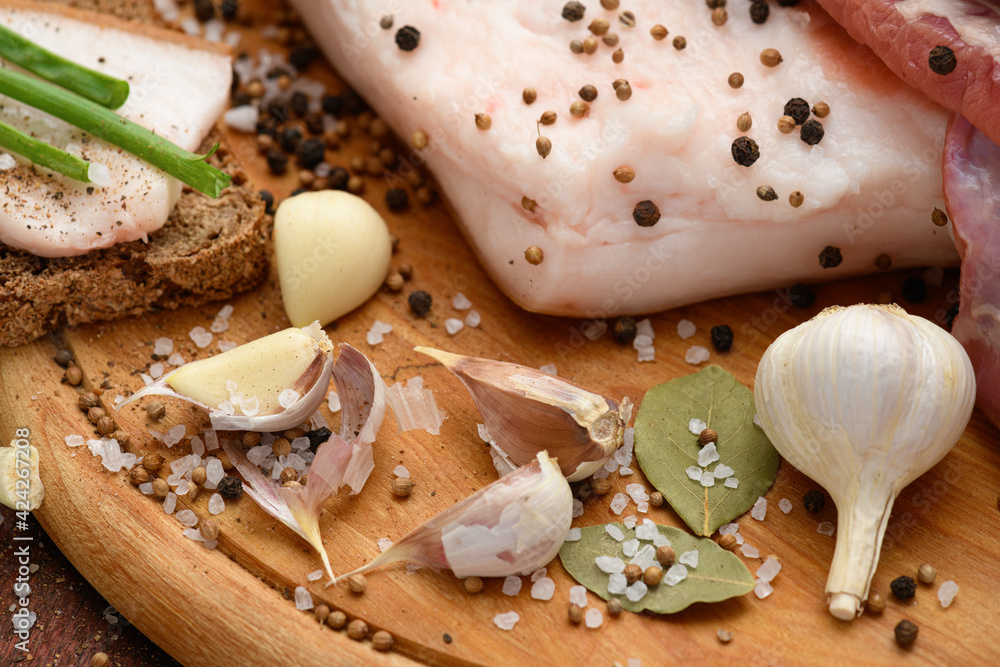 raw pork meat and lard with salt, spices and garlic on a cutting board, dark wooden background