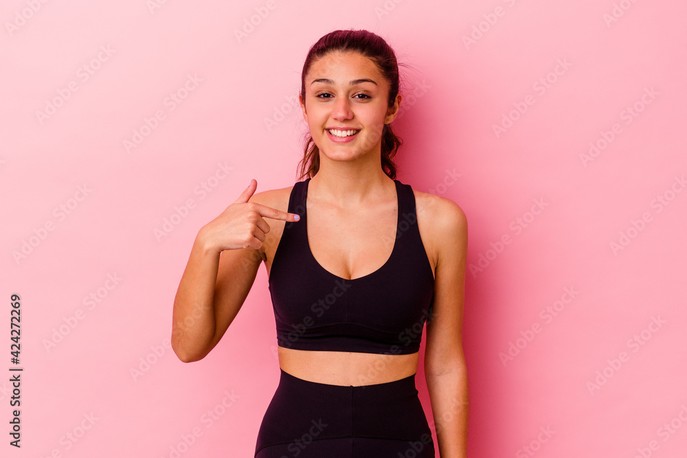 Young sport Indian woman isolated on pink background person pointing by hand to a shirt copy space, proud and confident