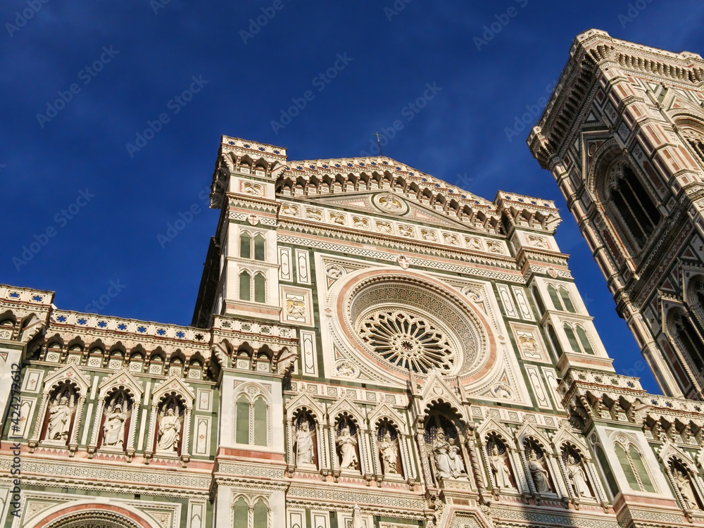 Cathedral of Santa Maria del Fiore. Landmark 1200s cathedral colored marble facade and Giotto tower close sunny view with blue sky background. Travel Italy