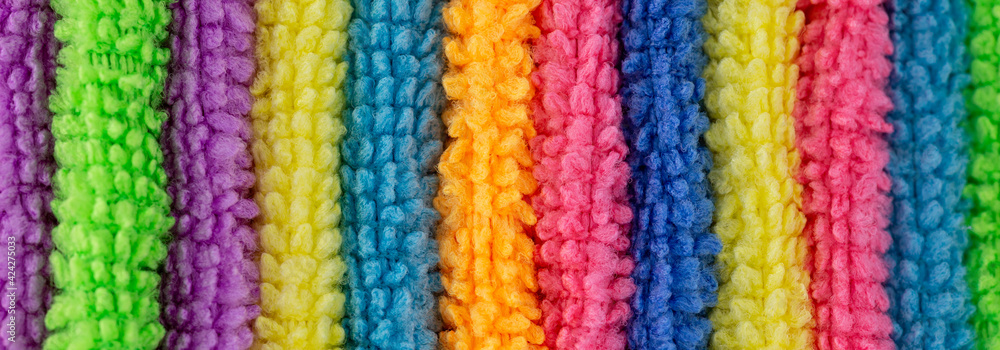 Towels in various colors as background to the topics spa, wellness and hygiene with the colors yellow, blue and pink in panorama format