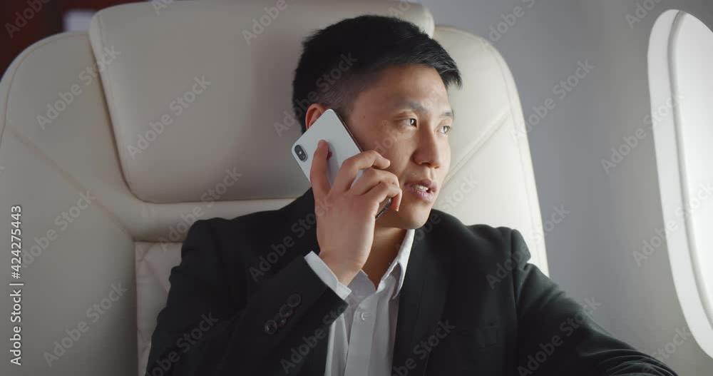 Asian businessman talking by phone on board of modern private airplane Asian businessman talking by phone on board of modern private airplane