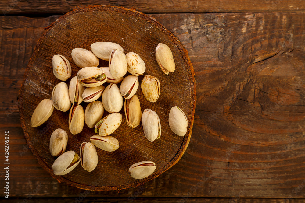Fototapeta premium Pistachio nuts scattered on a round board on a wooden table.