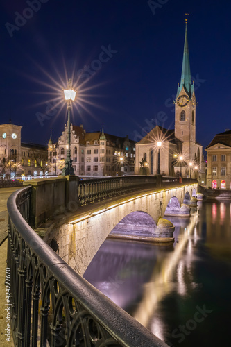 View over bridge and the water of the lake at Fraumunster Church in Zurich, Switzerland in the blue hour night time
