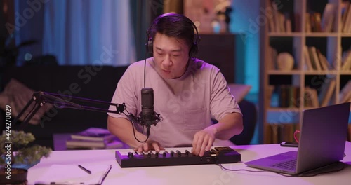 Inspired Asian Male Artist Singing into Microphone Recording Electronic Audiotrack on Piano Synthesizer Enjoying Staying Home Late at Midnight. photo