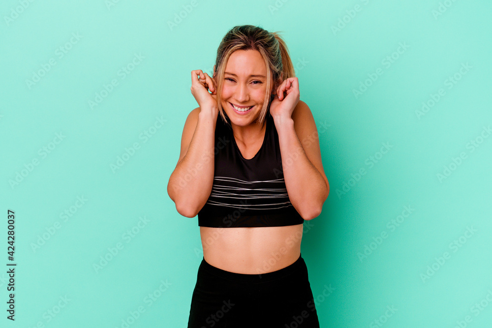 Young caucasian sport woman isolated on blue background covering ears with hands.